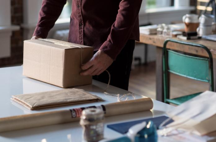 Man in a maroon button up shirt lifts cardboard box