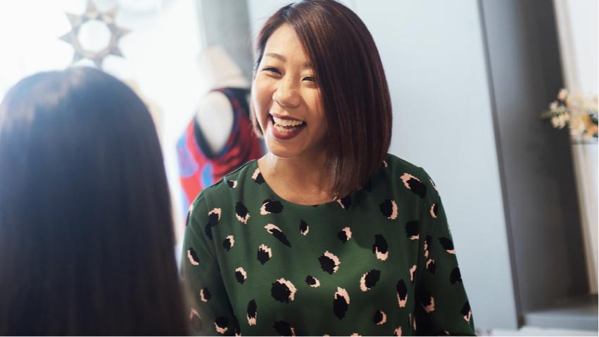 A happy female Small Business owner with a black bob hairstyle and a green shirt with black and white print.